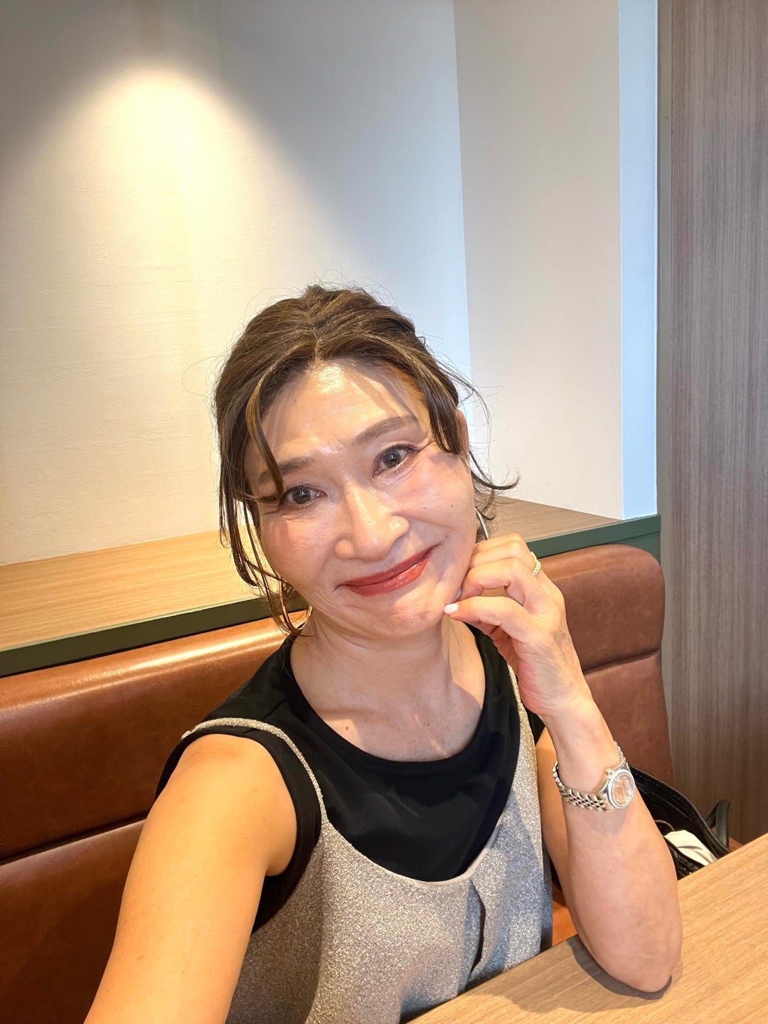 黒いトップスとシルバーのキャミソールを重ね、笑顔で椅子に座る女性
