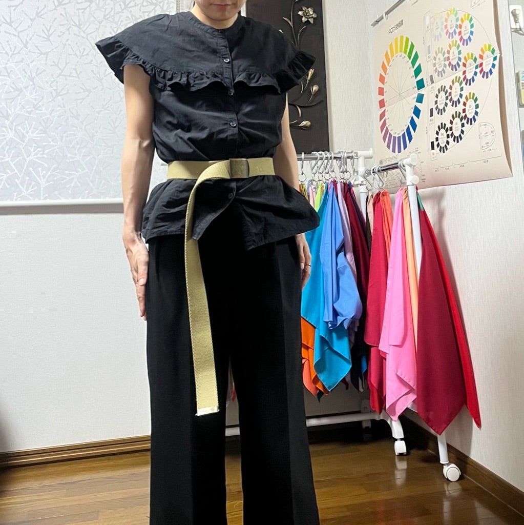 黒いフリルトップスとワイドパンツをゴールドベルトで整えた女性