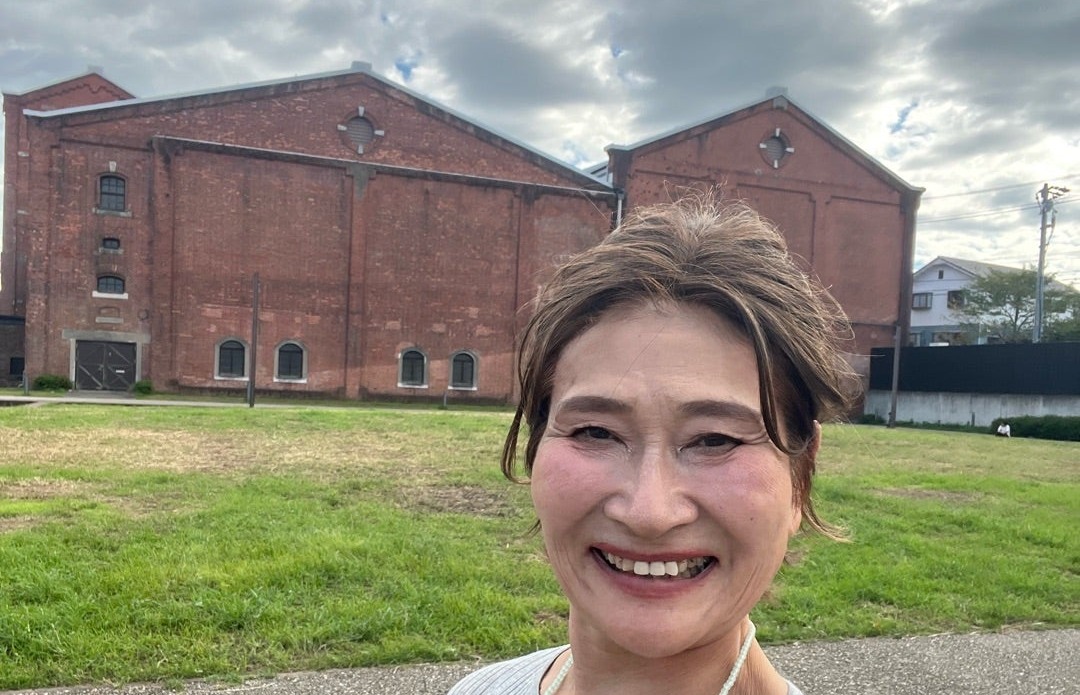 半田赤レンガ建物を背景に笑顔を見せる三村由香
