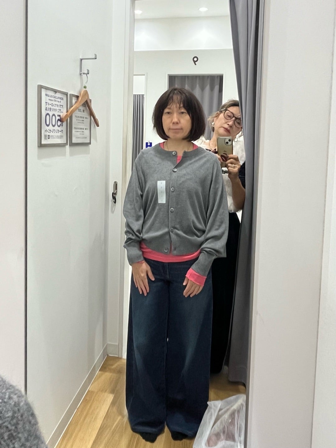 グレーのトップスとピンクの重ね着を鏡で確認する様子