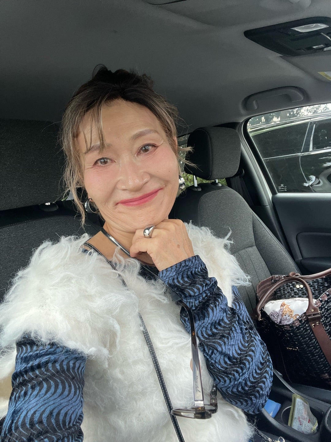 白い毛足のあるベストと青い柄のトップスを着た由香さん