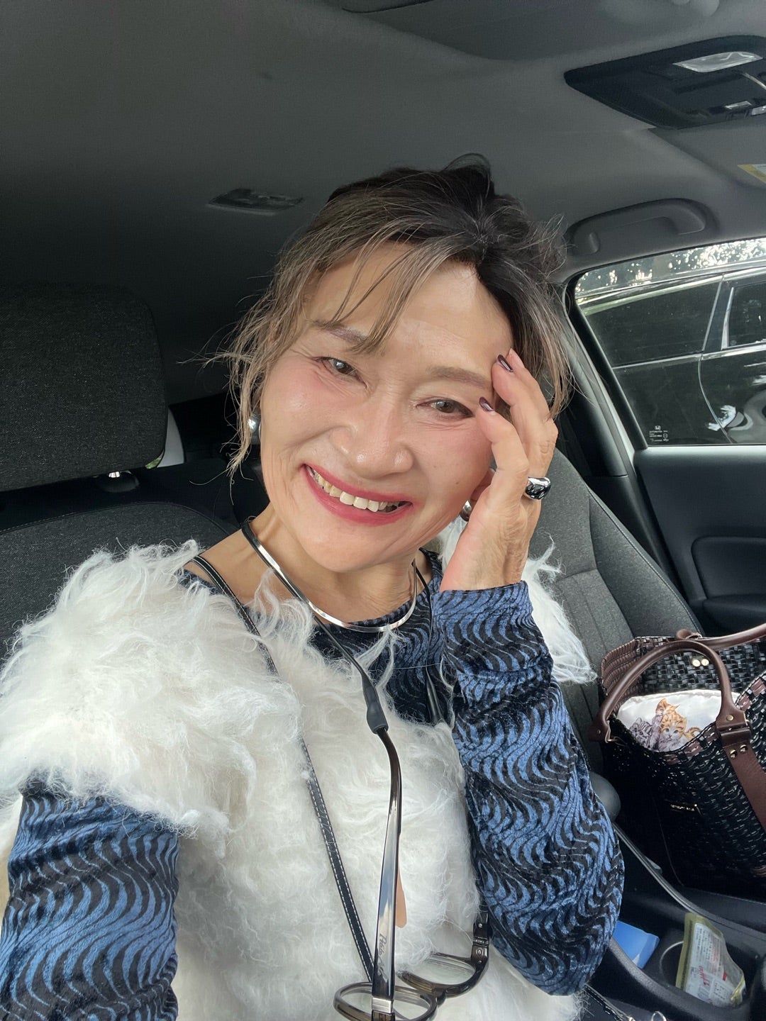 白いベストと青い柄のトップスを合わせて笑う由香さん