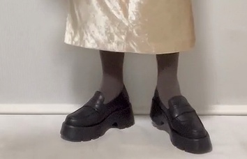光沢のあるスカートにグレーのタイツと黒いローファーを合わせた足元