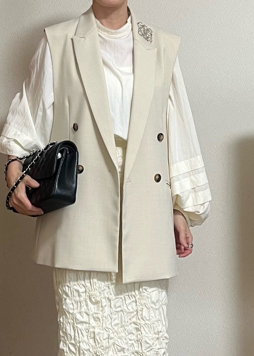 白系の服にジレと黒いバッグを合わせた装い